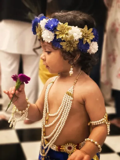 A profile shot of the child dressed as Krishna, holding a flower. The soft focus and checkered floor create a beautiful, timeless portrait.