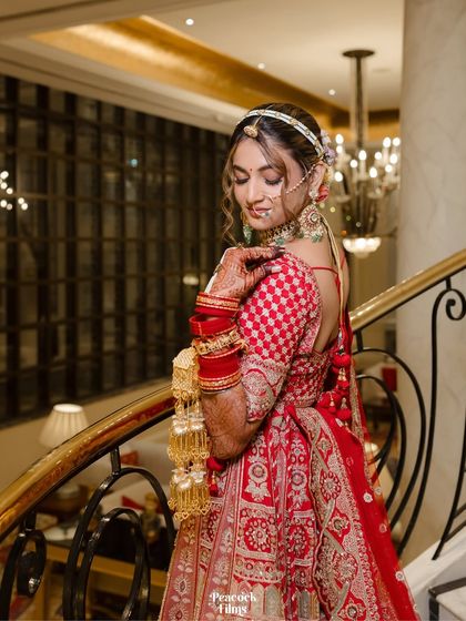 The bride poses on a grand staircase, her hand resting on the railing. The elegant setting complements her sophisticated bridal look.