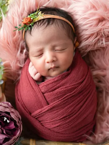 There is nothing more precious than a sleeping newborn. I specialize in safe newborn posing, and this little one, nestled among flowers in a deep red wrap, shows the peaceful, dreamy art we can create in those first few weeks.