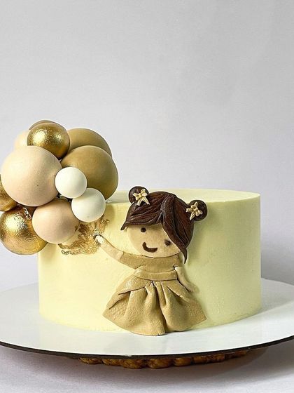 A simple and sweet cake featuring a little girl holding a bouquet of balloons. The figure is created with layered fondant for a 2D effect, and the balloons are made from chocolate spheres.