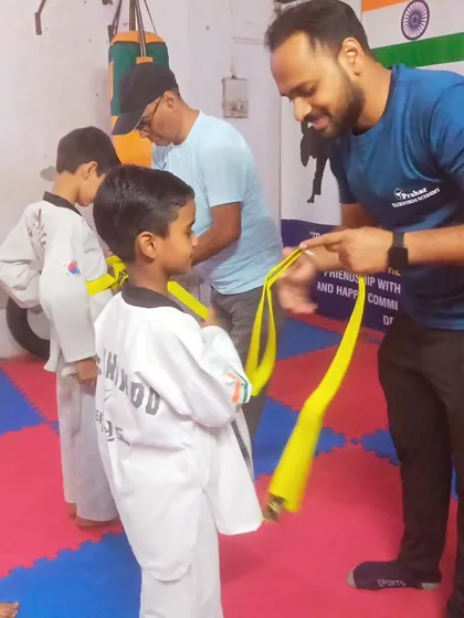 A coach carefully ties a new yellow belt, explaining the significance of this milestone to a young student.
