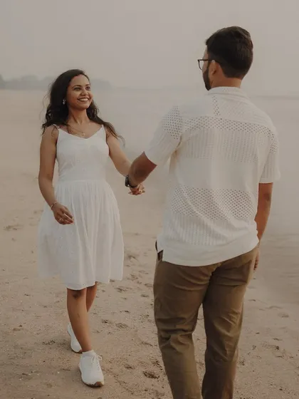 A candid moment of a couple walking hand-in-hand on the beach. Her smile says everything about the love and happiness they share.