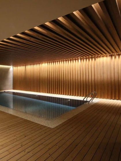Another view of this luxurious indoor pool area, highlighting the warm ambient lighting and the floor-to-ceiling wood cladding on the walls, creating a spa-like atmosphere.