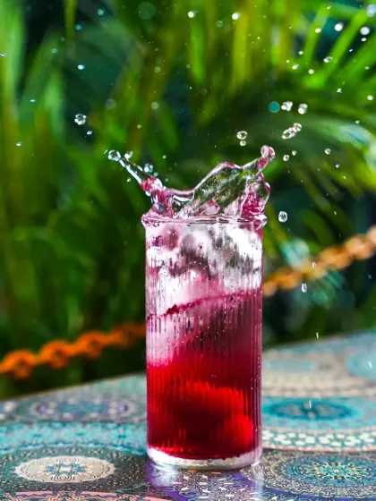 An energetic splash captured in a glass of deep red liquid against a vibrant green, leafy background. This action shot is perfect for conveying a sense of refreshment and excitement for any beverage brand.