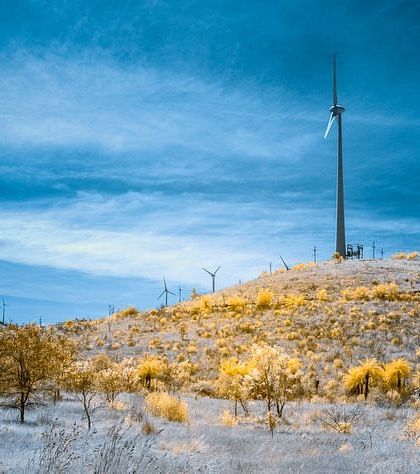 A windmill on a hill, photographed in infrared. The vegetation appears white and yellow against a dramatic dark blue sky, creating a stark and surreal image.