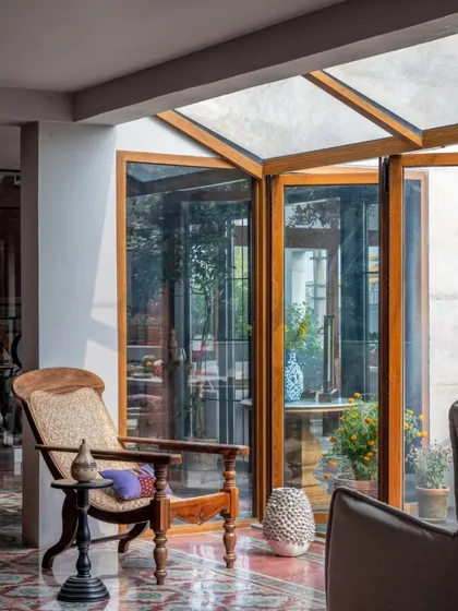 Sunlight streams into this sitting area, highlighting the textures of the woven chair and the smooth, patterned floor. This space was designed as a transitional zone, a place to pause and enjoy the connection to the lush greenery just outside the folding glass doors.