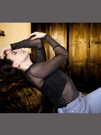 A cozy and intimate portrait of a model in a sheer top, relaxing in a warmly lit home environment.