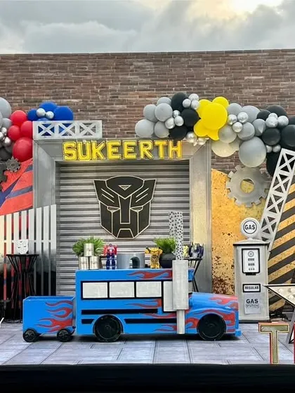 An action-packed Transformers party stage, showcasing both Optimus Prime and Bumblebee with industrial-style props, cityscapes, and bold balloon arrangements.