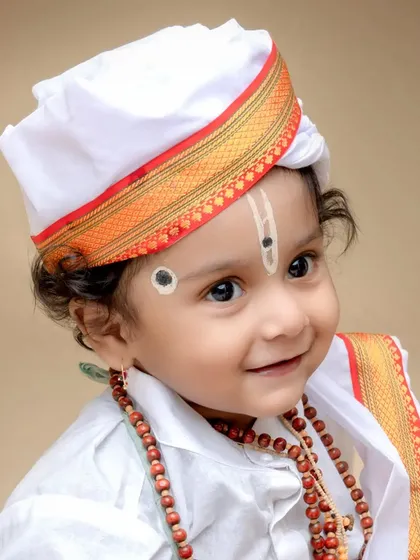 A gentle and sweet portrait of a baby Varkari. The focus is on the child's innocent expression, highlighted by the traditional turban and rudraksha necklace.