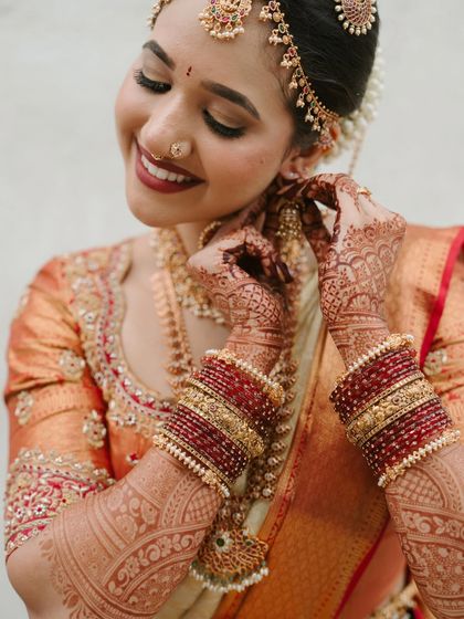A candid moment of the bride adjusting her earring. This shot highlights the intricate details of her henna, the beautiful jewellery, and the soft, natural finish of her makeup.