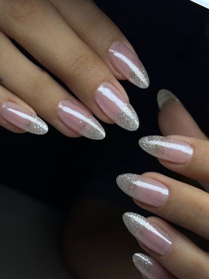 An elegant glitter ombré on almond-shaped nails. The silver glitter is concentrated at the tips and fades softly into the sheer nude base.