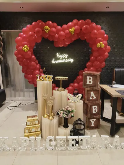 Make a bold statement with a custom heart-shaped balloon arch. This dramatic red balloon heart, paired with a glowing 'Happy Anniversary' neon sign and personalized light-up names, creates a stunning focal point for your celebration.