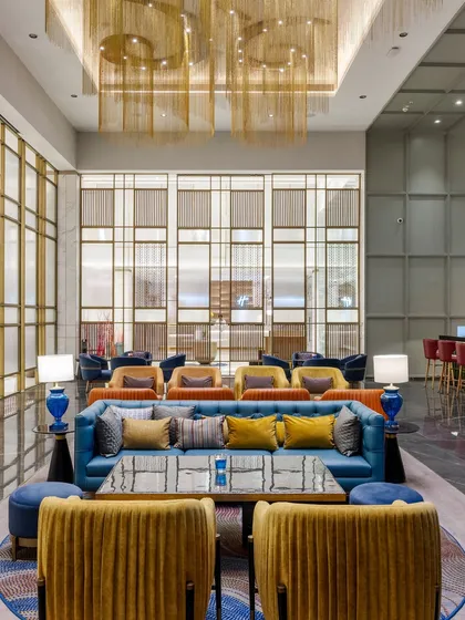 The vibrant lounge at Holiday Inn, Lucknow, showcasing a dynamic interplay of color and texture. We designed this public space with varied seating arrangements, from plush blue sofas to mustard yellow armchairs, to foster social interaction while intricate metal screens provide a sense of privacy.