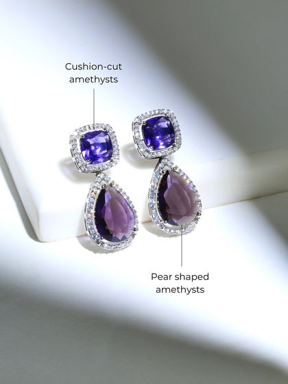 A detailed look at the amethyst earrings, featuring cushion-cut and pear-shaped amethysts. Each stone is haloed by diamonds to enhance its deep purple hue.