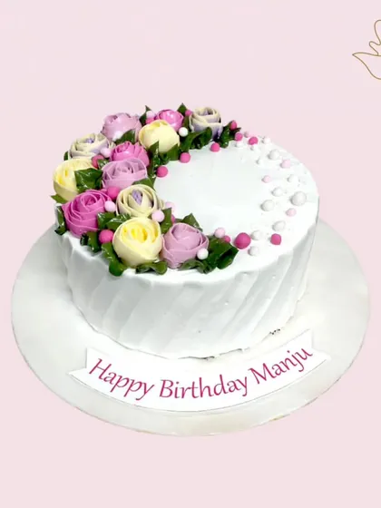A beautiful floral cake with a half-wreath of buttercream roses in shades of pink, lavender, and cream. This design is both elegant and charming.