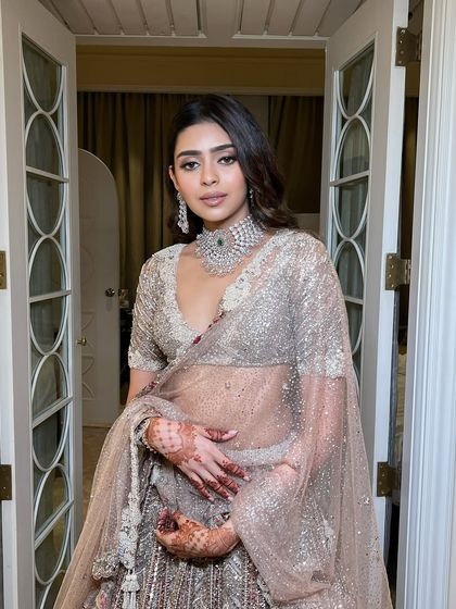 A full-length view of the bride in her rose gold lehenga. The soft, ethereal makeup perfectly complements the delicate sparkle of the outfit, creating a look that is pure fairytale.