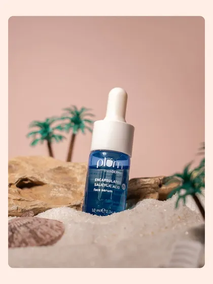 A skincare serum placed among sand, rocks, and miniature palm trees. The composition creates a mini-landscape that tells a story of a tropical escape.