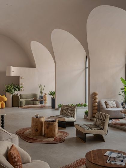 The large arched window floods the "Vaultz's Up" space with natural light, highlighting the smooth texture of the stucco walls and the organic shapes of the furniture.