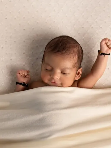 A sleepy stretch from a newborn tucked under a cream-colored blanket. This candid moment captures the sweet, unposed movements of a baby.
