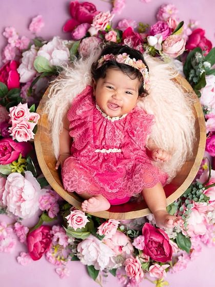 A happy baby girl in a basket of pink flowers. This overhead shot creates a beautiful floral frame around her, like a little pixie.