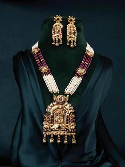 A slightly different angle of the traditional necklace set on a bust, captured against a dark green background to make the gold details pop.