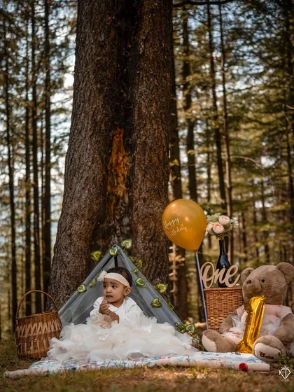 A portrait of the little one sitting proudly amidst her birthday setup, with tall pine trees in the background. This image showcases the unique Pahadi vibe of my outdoor sessions in Shimla.