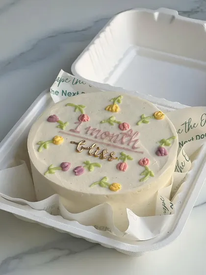 A sweet and delicate mini cake celebrating a one-month milestone. It's decorated with tiny, hand-piped tulips in soft pastel colors.