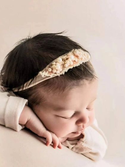 A close-up of a sleeping newborn, showcasing the delicate features and peaceful expression. The soft headband adds a subtle, sweet detail to this gentle portrait.