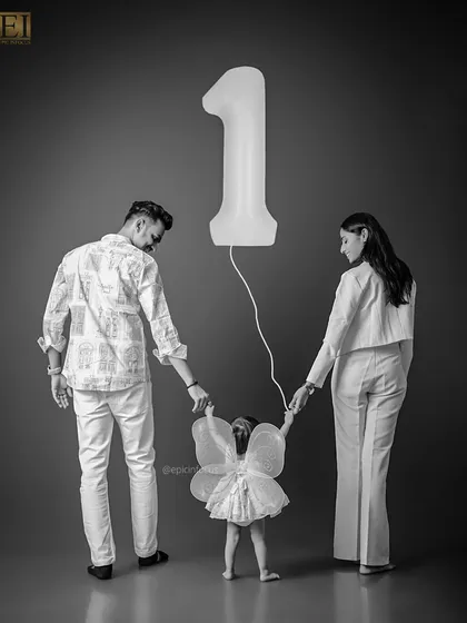 A beautiful black and white family portrait celebrating a first birthday. The parents hold their little fairy's hands, symbolizing their guidance as she takes her first steps into a new year.