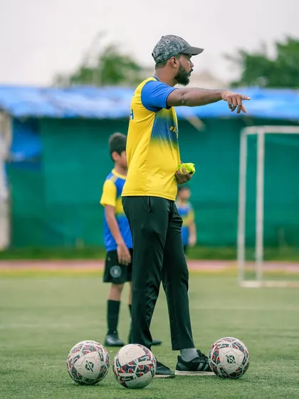 A coach stands on the pitch, pointing and directing his players. This image is accompanied by a powerful message defining the many roles a Bravo coach plays, from teacher and mentor to a second family for your child.