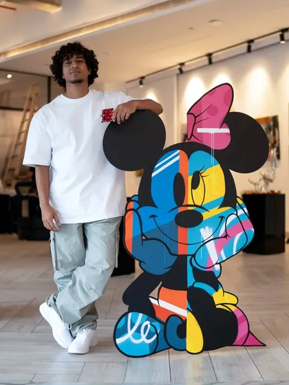 Standing with my finished Minnie Mouse artwork. This piece is huge, standing 55 inches tall, and uses vibrant spray-painted colors on layered MDF to bring her to life.