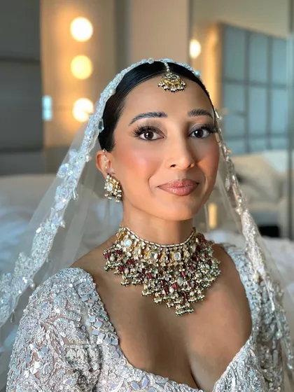 The complete bridal look with the veil placed over the sleek low bun. The simplicity of the hairstyle ensures it doesn't compete with the heavily embellished veil and outfit.