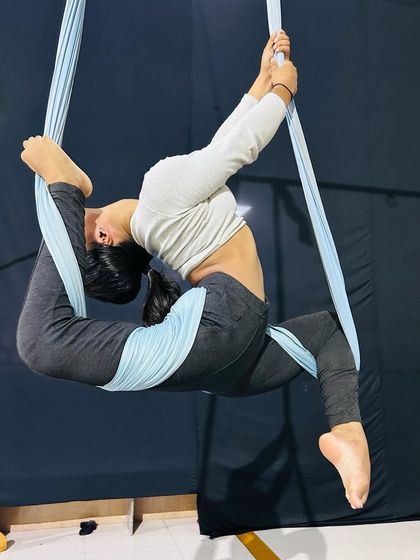 This advanced flexibility pose, a variation of a "scorpion," is made more accessible with the support of the aerial hammock.
