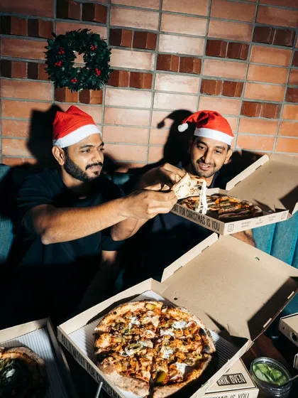 Merry Crustmas! The founders share a slice during the holidays, surrounded by pizza boxes ready for a festive feast.