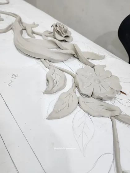 A raw clay sculpture of a floral design, laid over the initial sketch. This shows how the 3D form is built directly on top of the 2D drawing, translating the lines into tangible form.