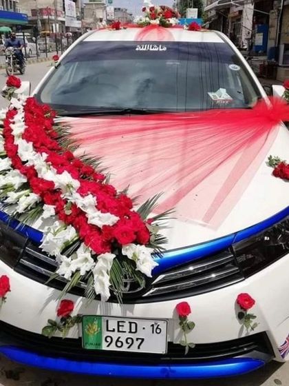 An elegant car decoration with a large bouquet of red and white flowers on the hood, complemented by a red fabric drape.