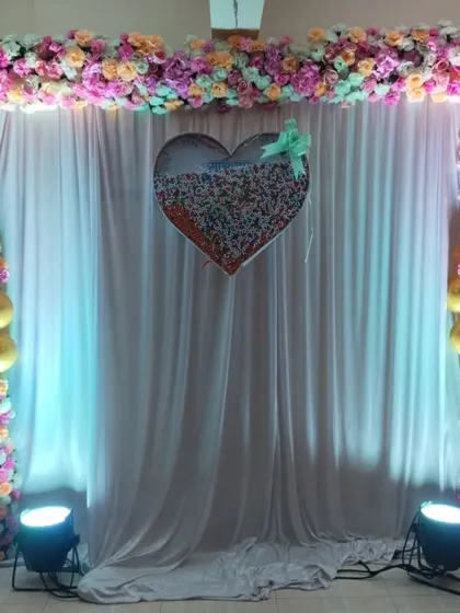 A simple yet elegant naming ceremony backdrop made with a floral frame, a white curtain, and a sequin heart centerpiece.