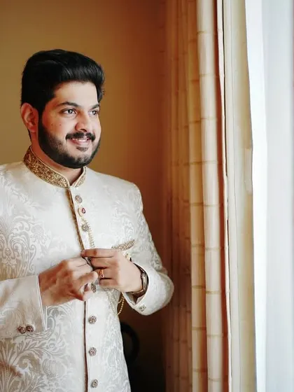 The groom getting ready by the window. This candid shot captures a moment of anticipation, with the natural light highlighting the details of his sherwani.
