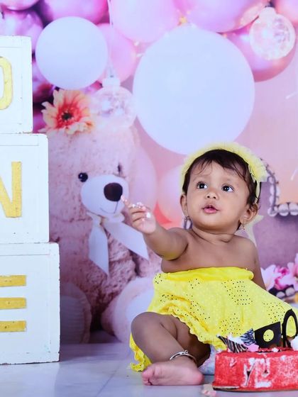 A baby girl enjoying her first birthday cake, dressed in a sunny yellow outfit.