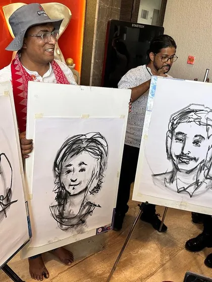 The final result of my live demo at the Pune art fair, holding up the three completed charcoal portraits.