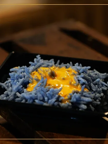 A plate of our visually stunning blue rice, topped with a savory yellow sauce. This dish is a testament to our creative and modern approach to global cuisine.
