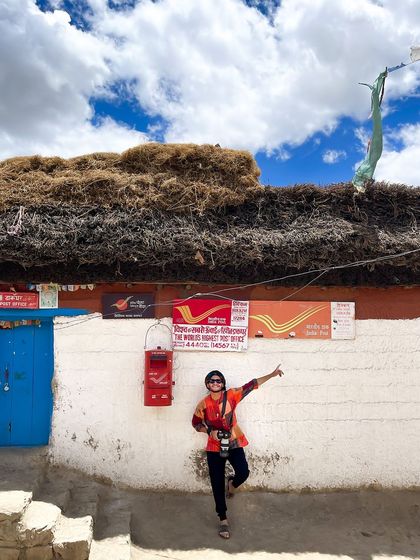 Posing next to the world's highest post office in Hikkim, Spiti Valley. This is a fun, iconic travel shot that documents a unique landmark and a memorable part of the journey.