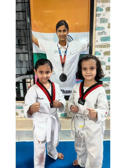 Two young girls in their Taekwondo uniforms, ready to train. Our classes provide a great space for kids to make new friends.
