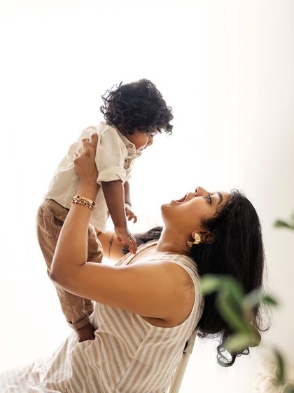 A beautiful high-key shot of a mother lifting her curly-haired son. The pure white background emphasizes their connection and his adorable curls.