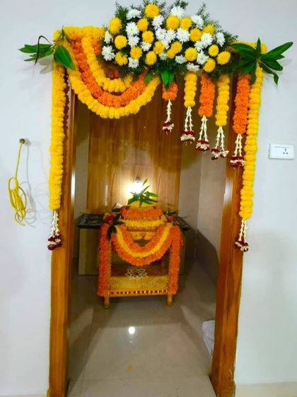 A flower decoration for a Griha Pravesh pooja area. The doorway to the pooja room is decorated with marigold garlands to create a sacred space.