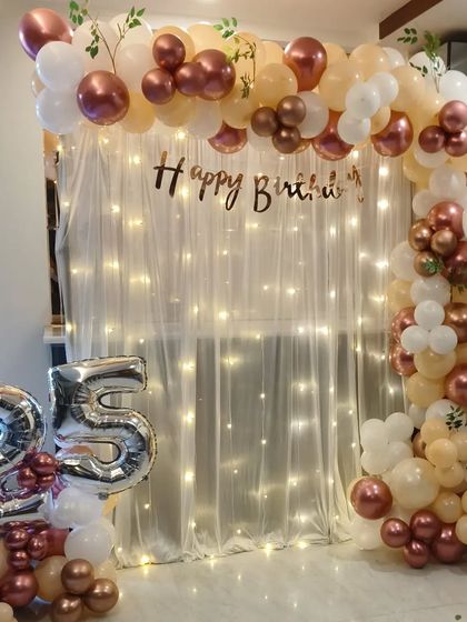 An elegant rose gold and peach theme for a 25th birthday. The balloon arch is set against a sheer curtain with fairy lights, creating a soft and beautiful effect.