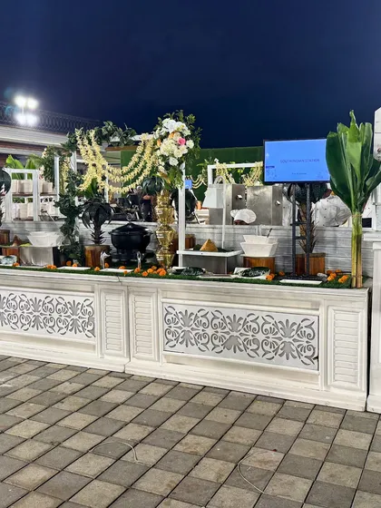A pristine white buffet station decorated with floral arches and traditional serving ware. This setup is perfect for an elegant daytime event or a sophisticated evening affair.