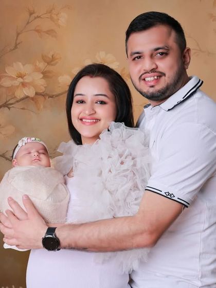 A happy family of three posing against a soft, floral backdrop. We offer various backdrops and styles to create classic family portraits that celebrate your new addition.