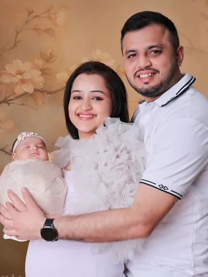 A happy family of three posing against a soft, floral backdrop. We offer various backdrops and styles to create classic family portraits that celebrate your new addition.