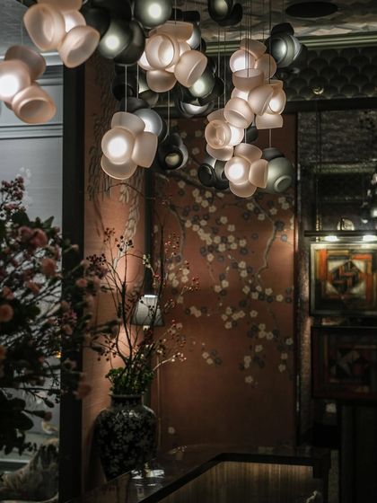 The organic forms of the Bocci 100 pendants complement the delicate floral patterns of the wallpaper, creating a rich, textured interior that balances modern design with traditional motifs.